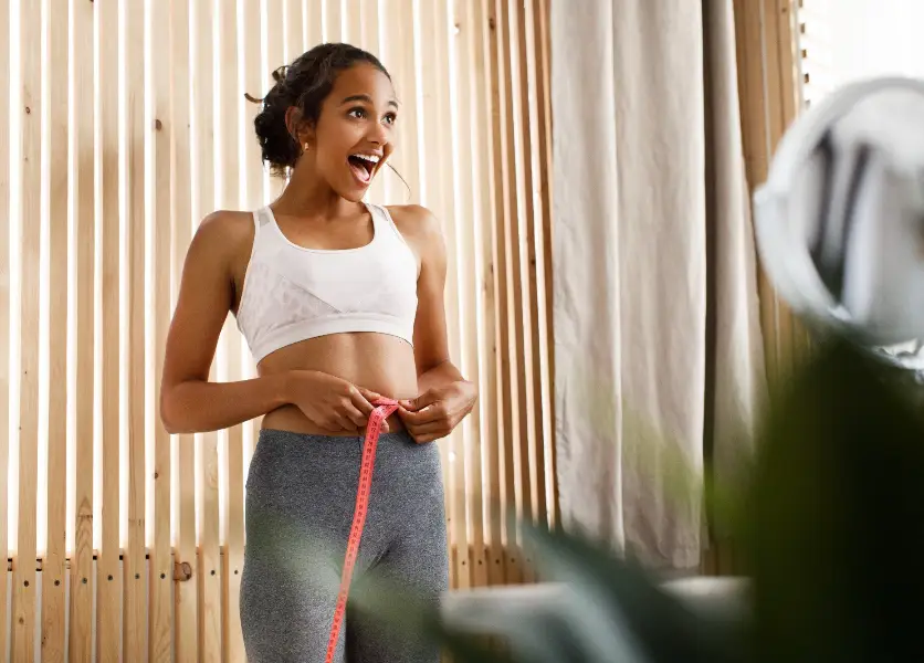 African woman is measuring her waist with a centimeter and has happy look